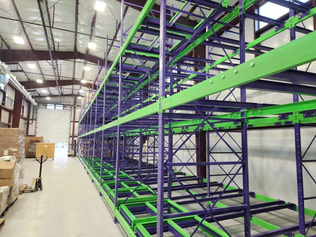 A row of push-back racking with green rolling carts and blue rails.