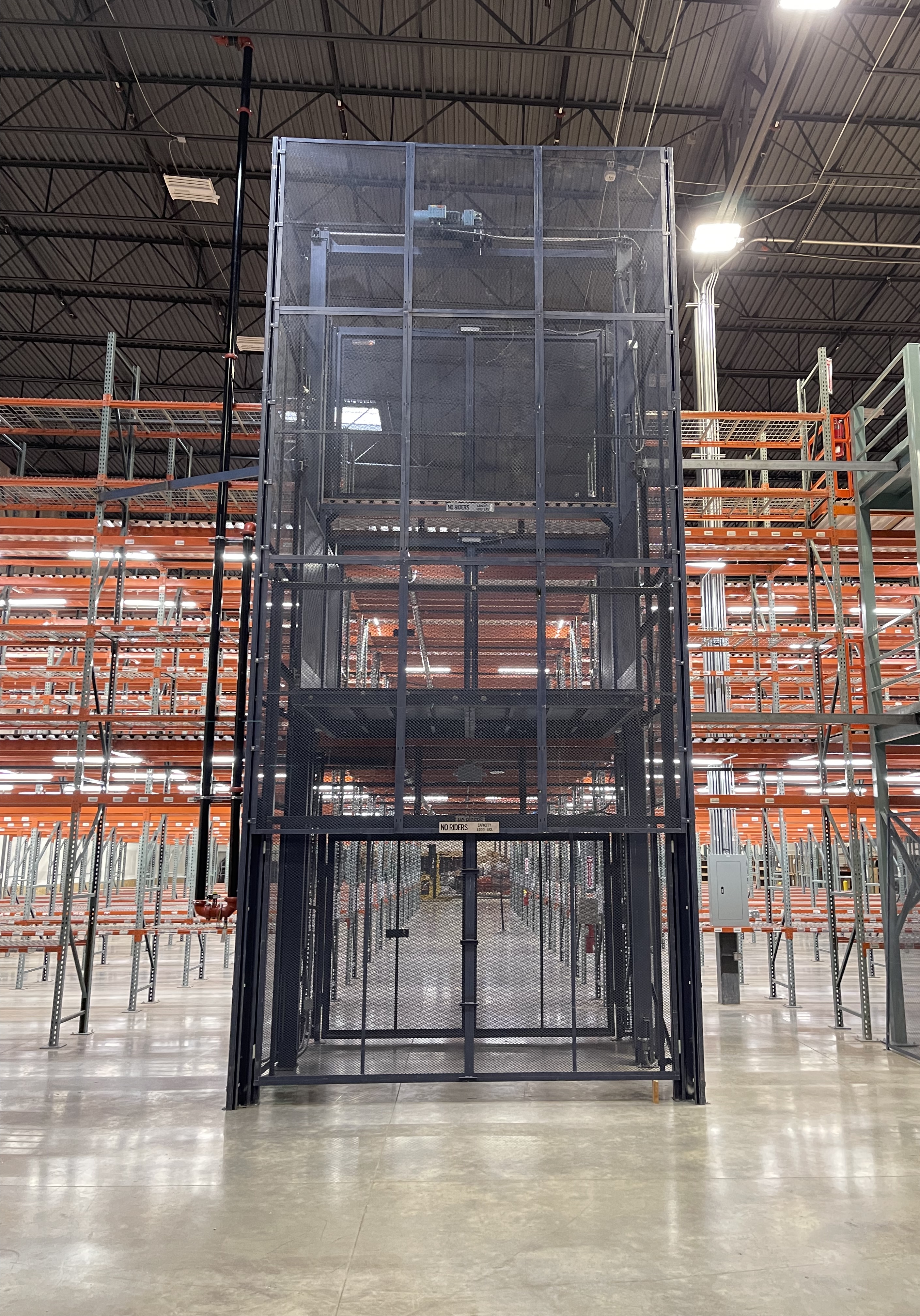 A black freight lift elevator against a large ledge and next to a staircase.