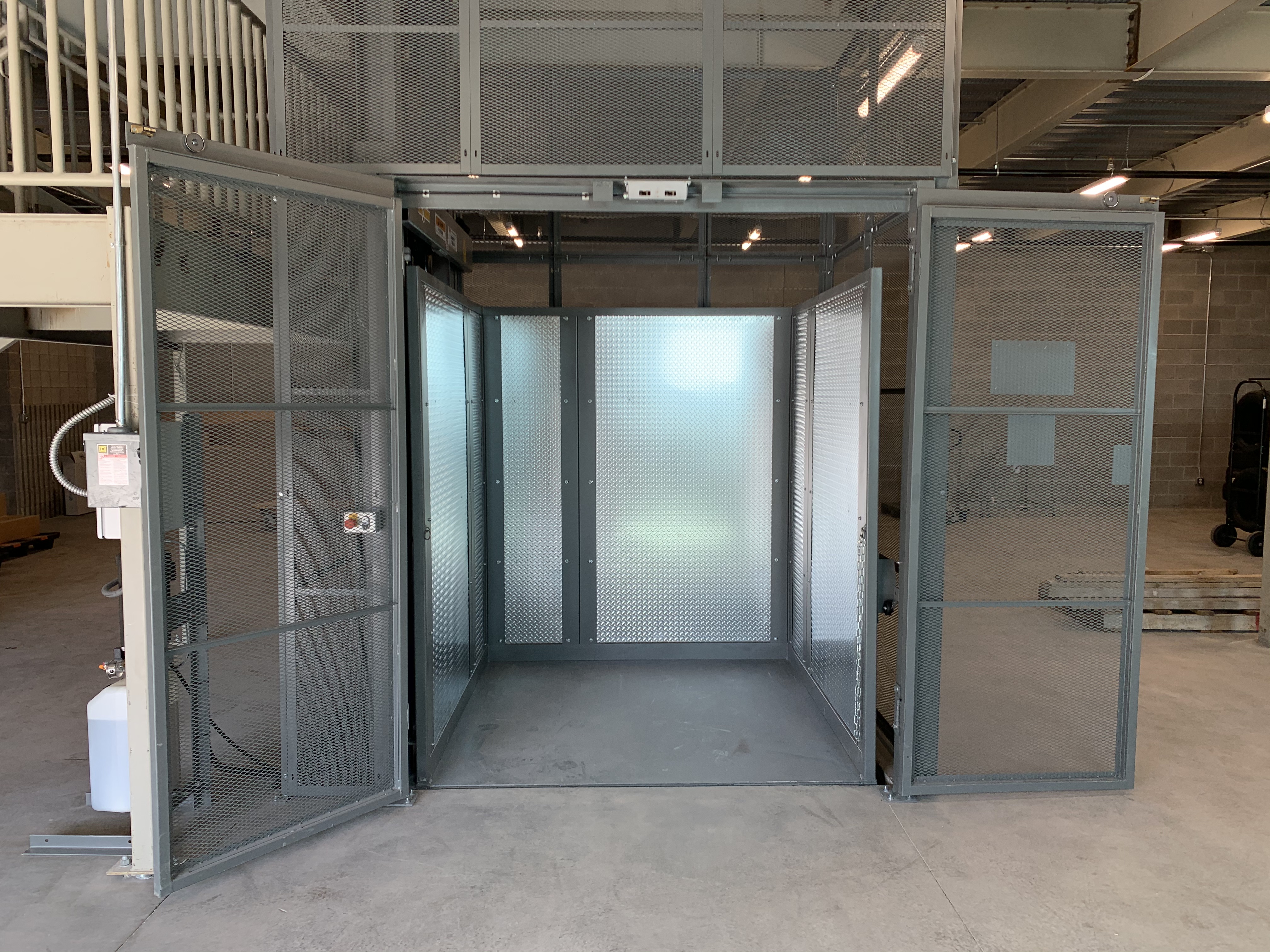 A black freight lift elevator against a large ledge and next to a staircase.